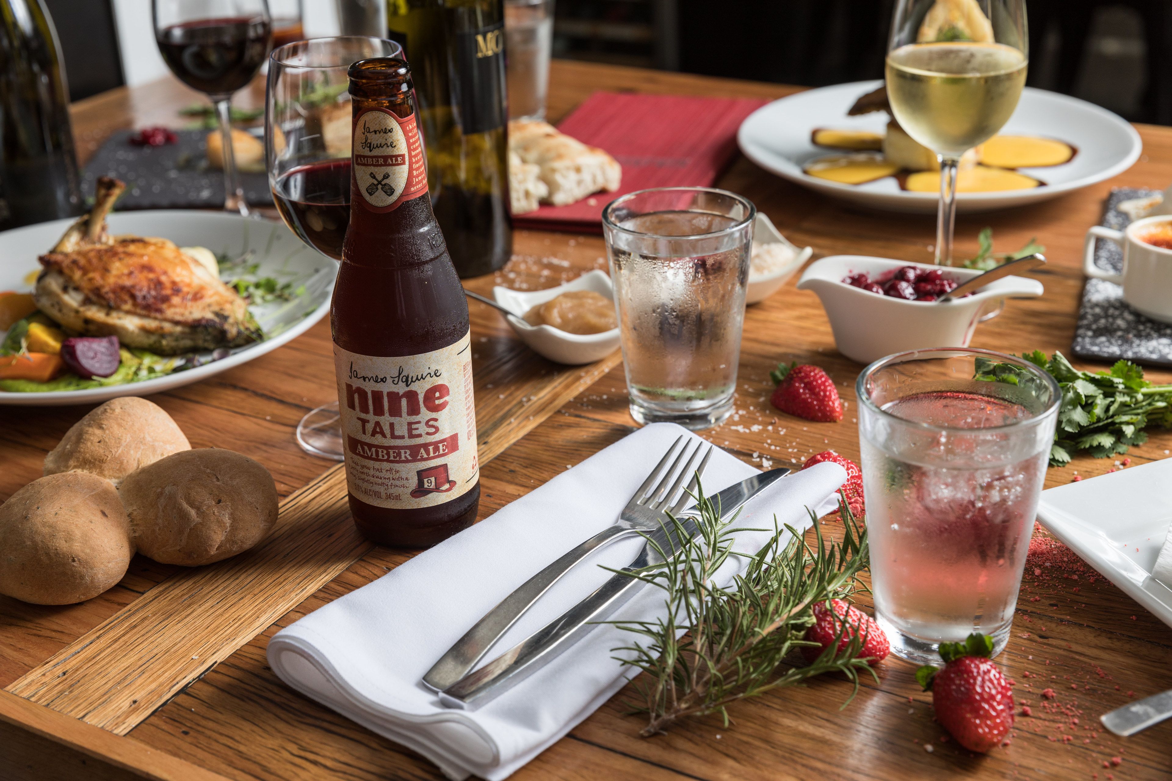 A dining table with a bottle of beer, a glass of wine, a plate of food, and a glass of water.