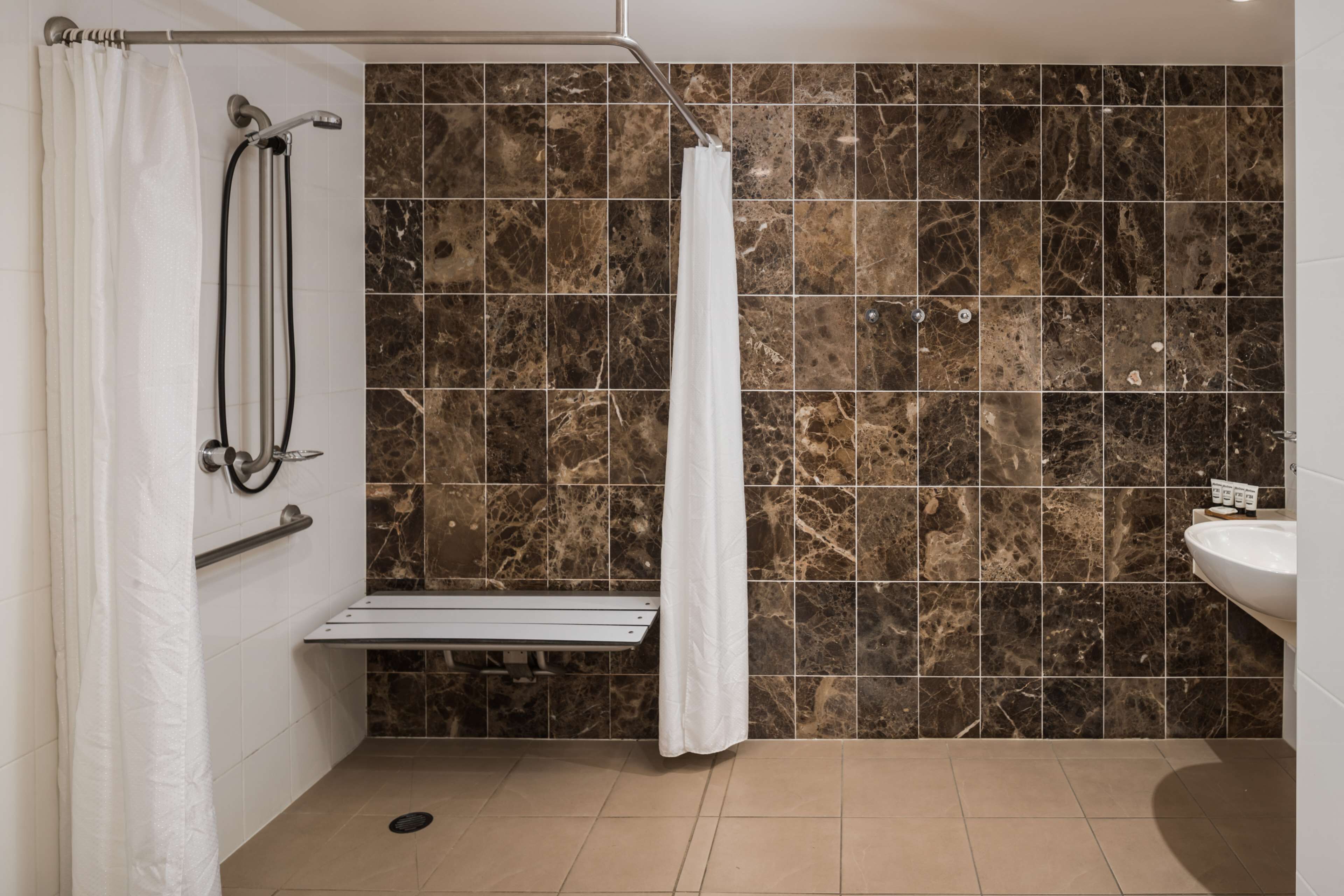 A modern bathroom with a shower, a bench, and a sink.