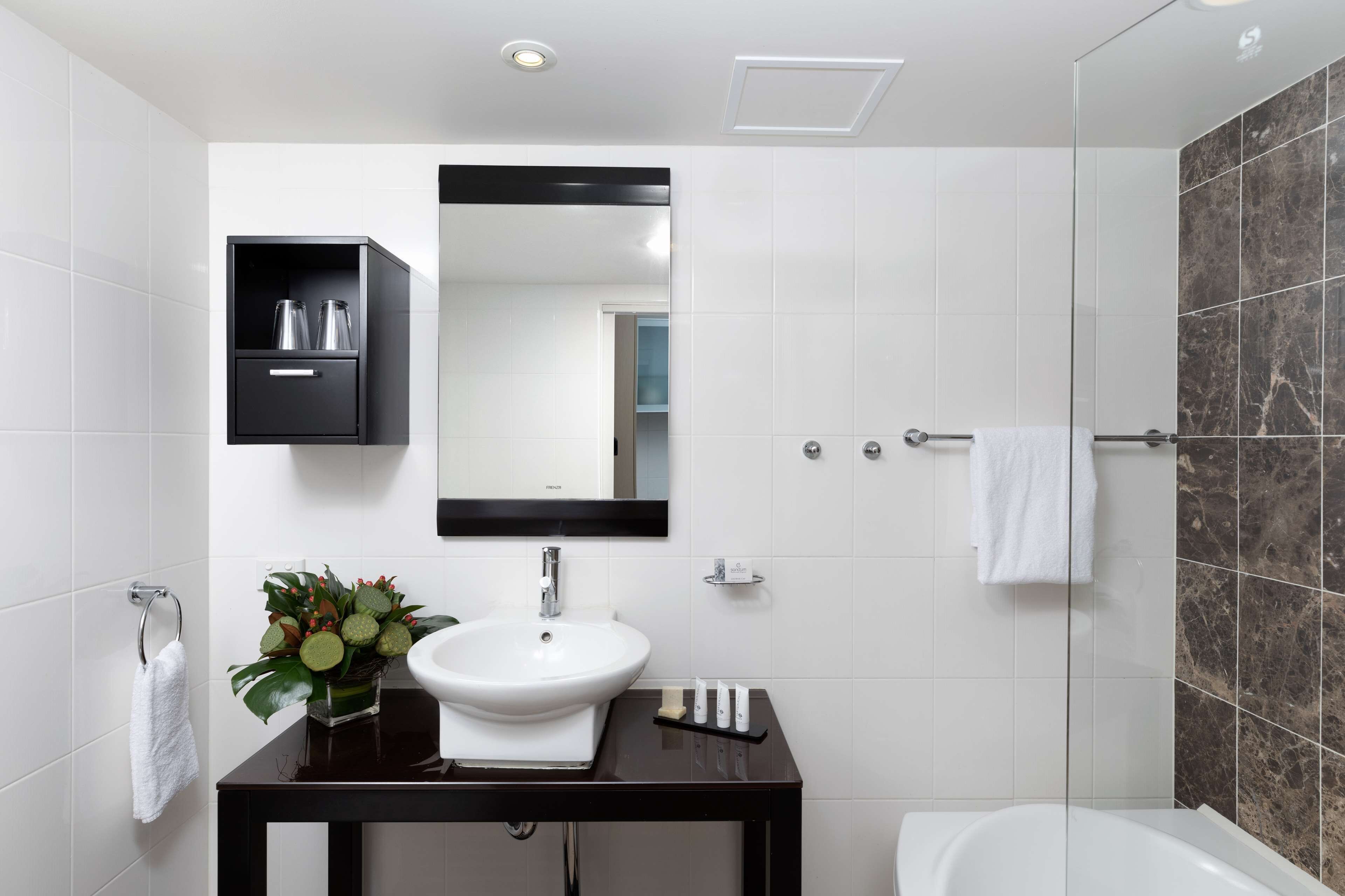 A modern bathroom with a white sink, dark vanity, and a glass shower enclosure.