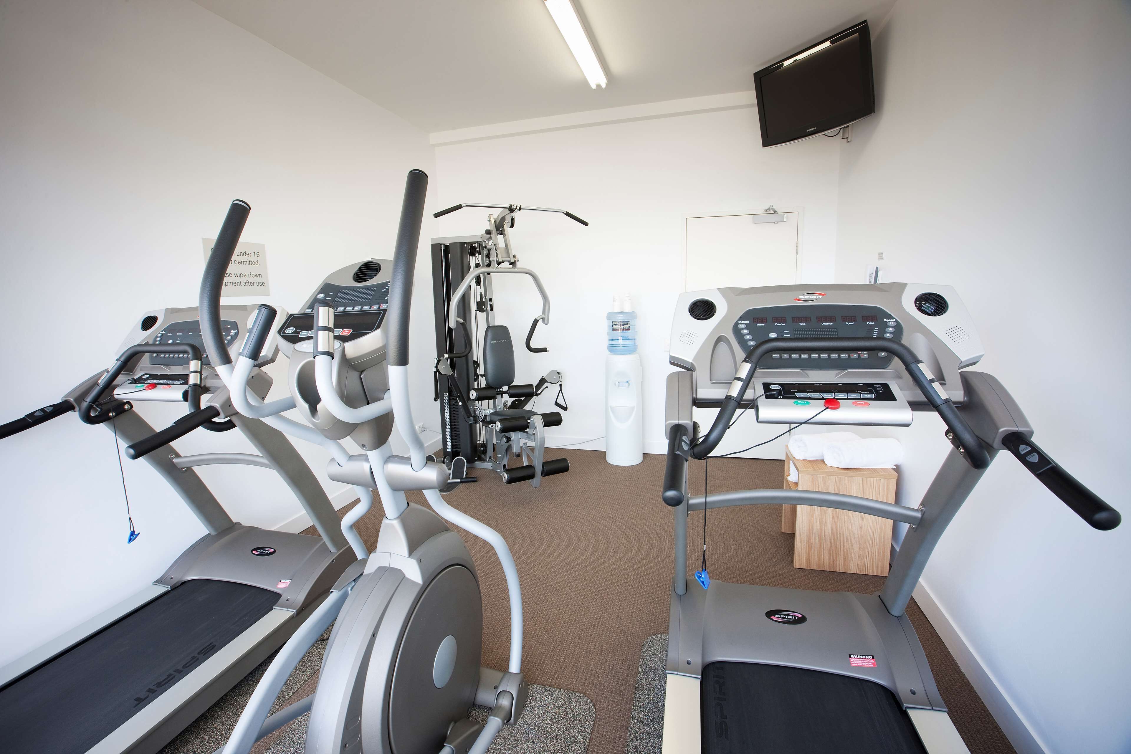 A gym with treadmills, elliptical machines, and a water dispenser.