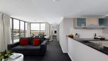 A modern living room with a dark grey sofa, red cushions, and a white coffee table. A kitchen area with a black countertop and white cabinets is visible to the right.