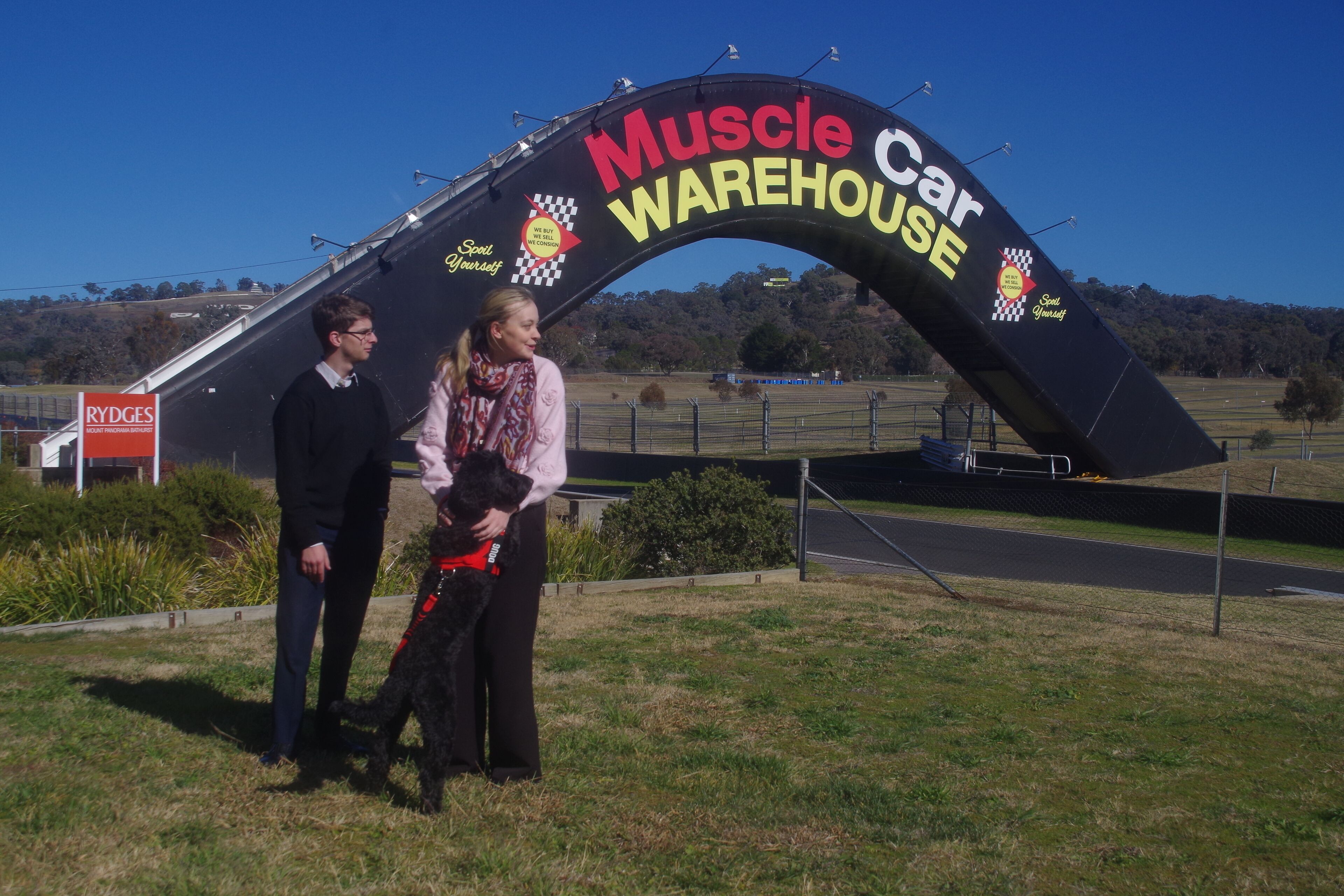 A large archway with the text 'Muscle Car Warehouse' and a checkered flag symbol.
