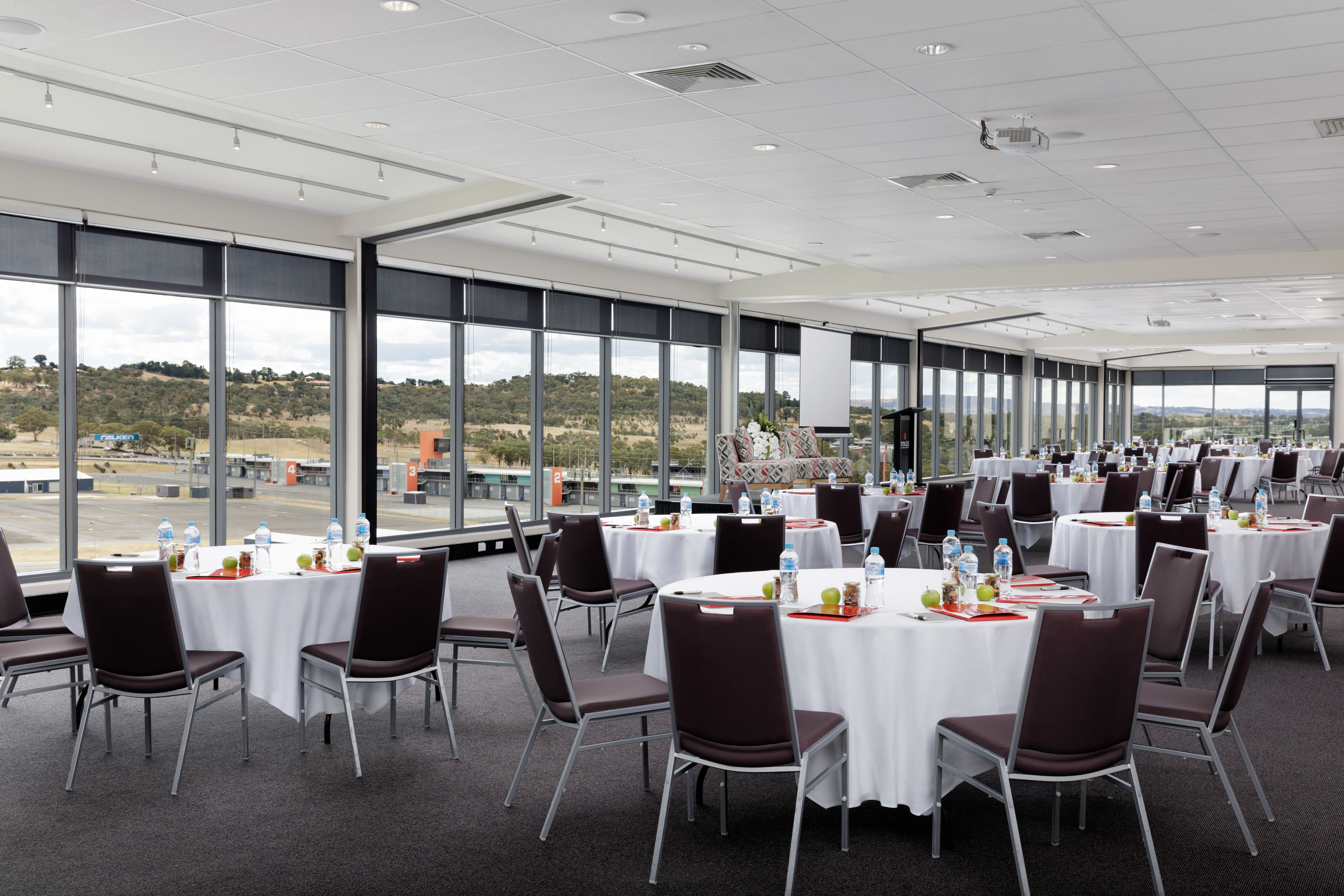 A spacious conference room with large windows, round tables, and modern chairs.