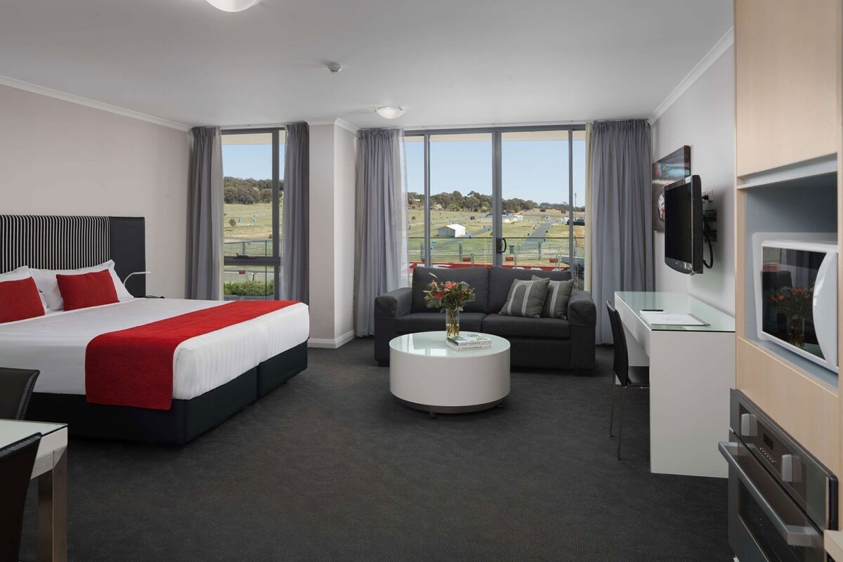 Habitación de hotel con cama, sofá, mesa de centro, televisor y vista a un campo de golf.