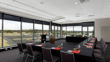 Sala de conferência com uma mesa comprida, cadeiras e vista para um aeroporto.
