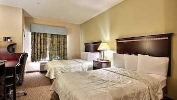 A hotel room with two beds, a desk, a chair, a lamp, and a window with curtains.