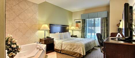 A hotel room with a large bed, a desk with a computer, a desk lamp, a telephone, and a window with curtains.