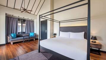 A four-poster bed with a grey headboard, a sofa with blue cushions, and a small table.