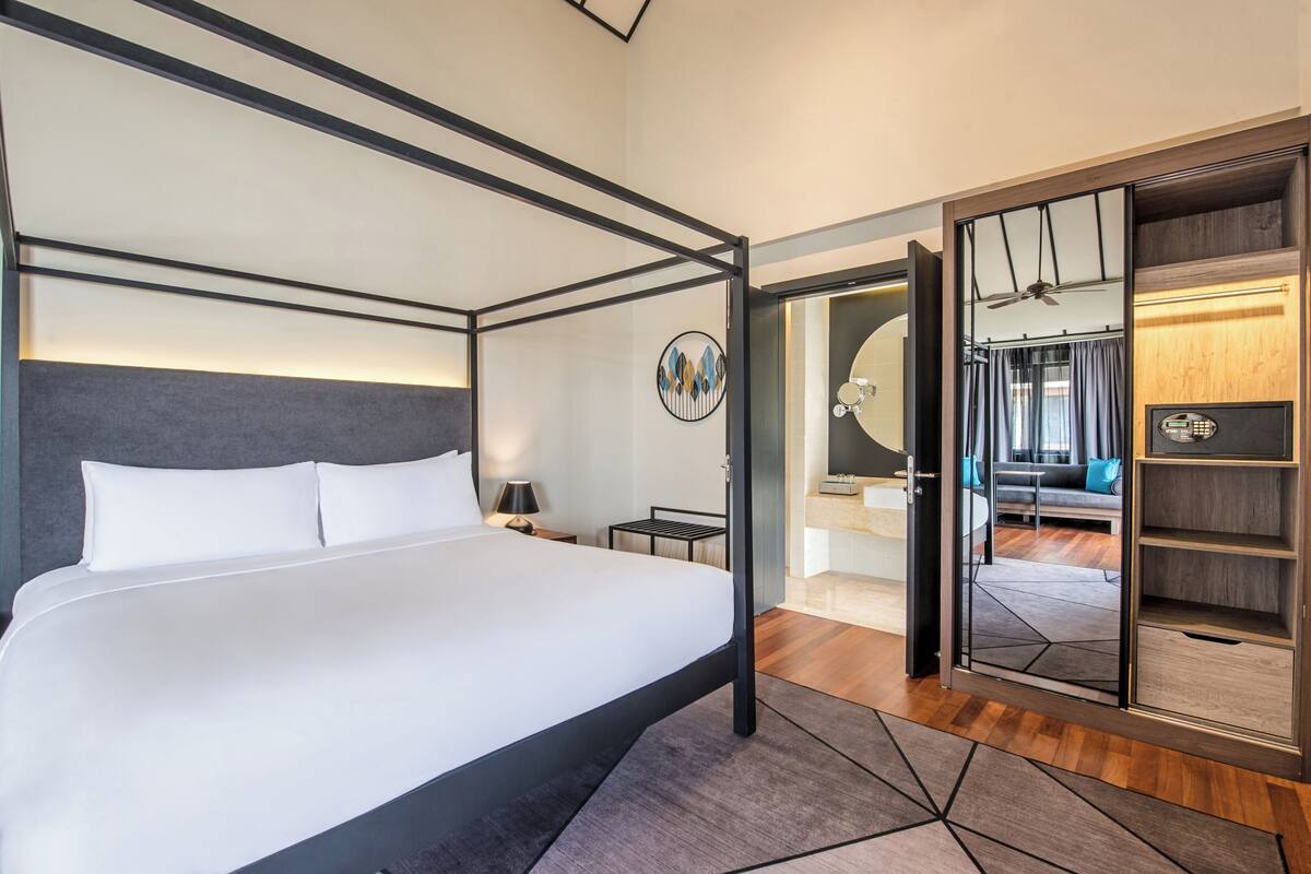 A modern hotel room with a four-poster bed, a walk-in closet, and a view into the living area.