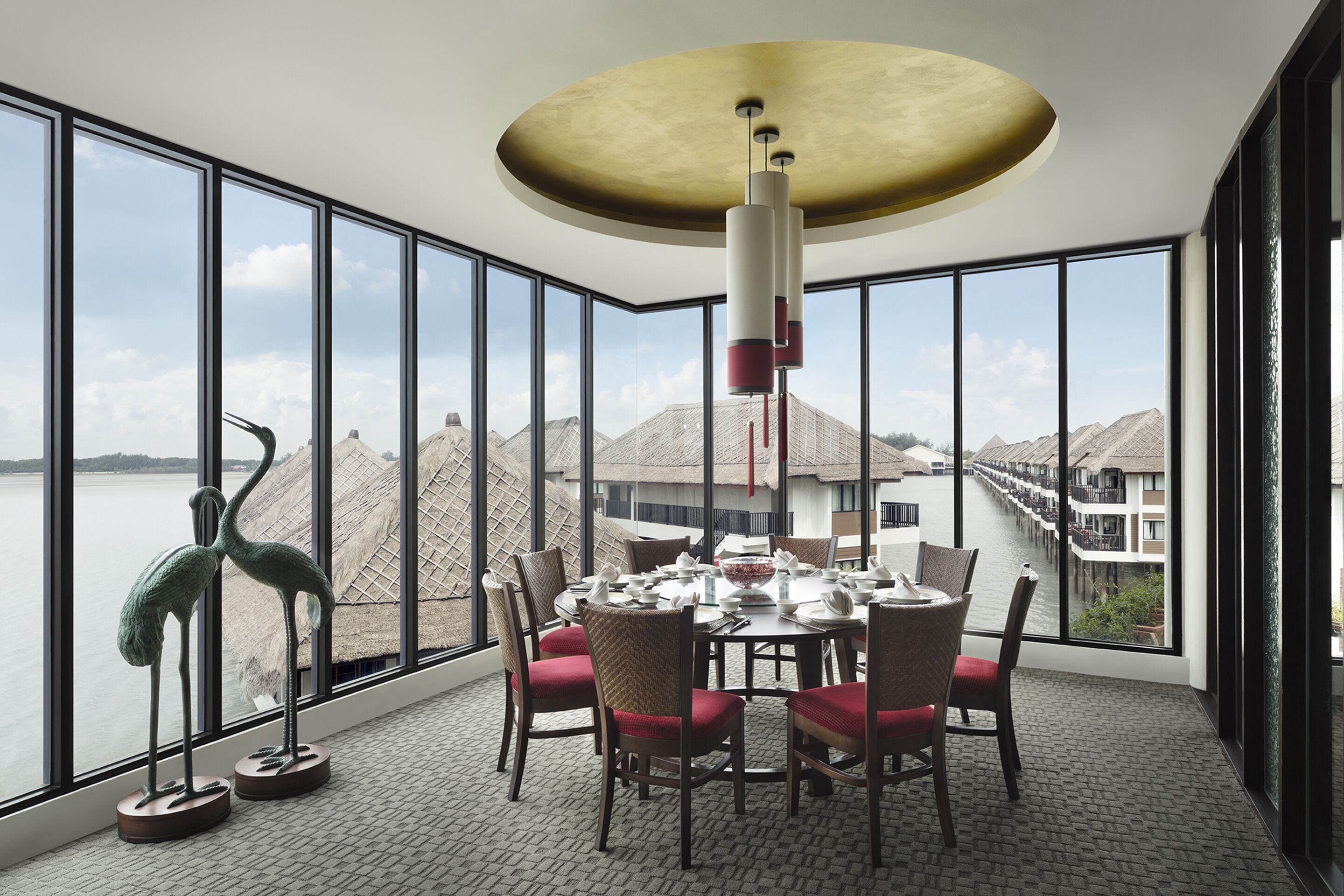 A dining area with a view of a water body and distant buildings, featuring a round table, chairs, and a decorative sculpture.