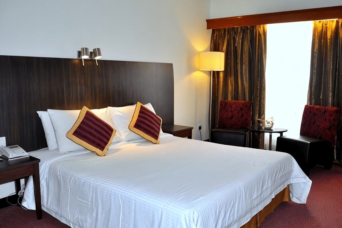 A hotel room with a large bed, a bedside table, a lamp, and two chairs.