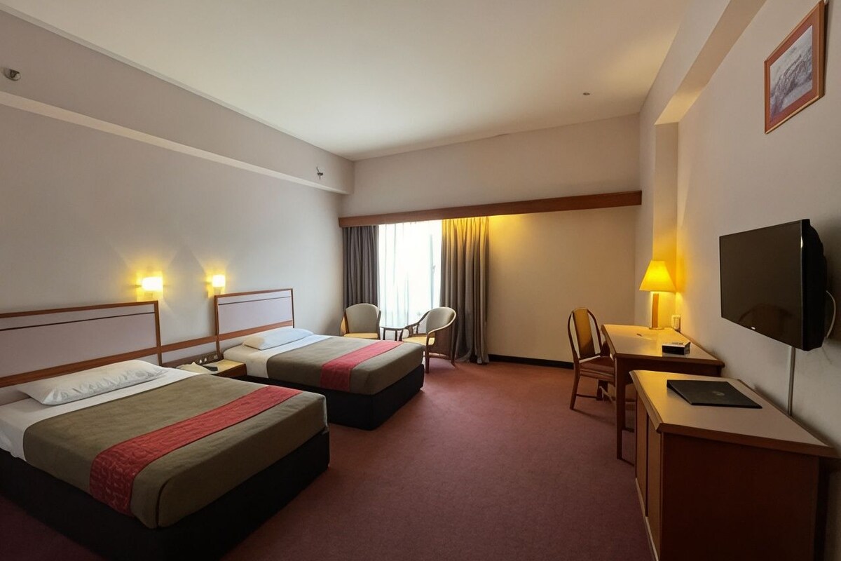 A hotel room with two beds, a desk, a chair, a TV, and a window with curtains.