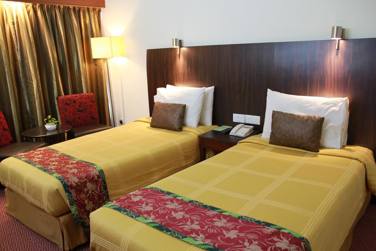 A hotel room with two beds, a nightstand, a lamp, and a small table with a plant.