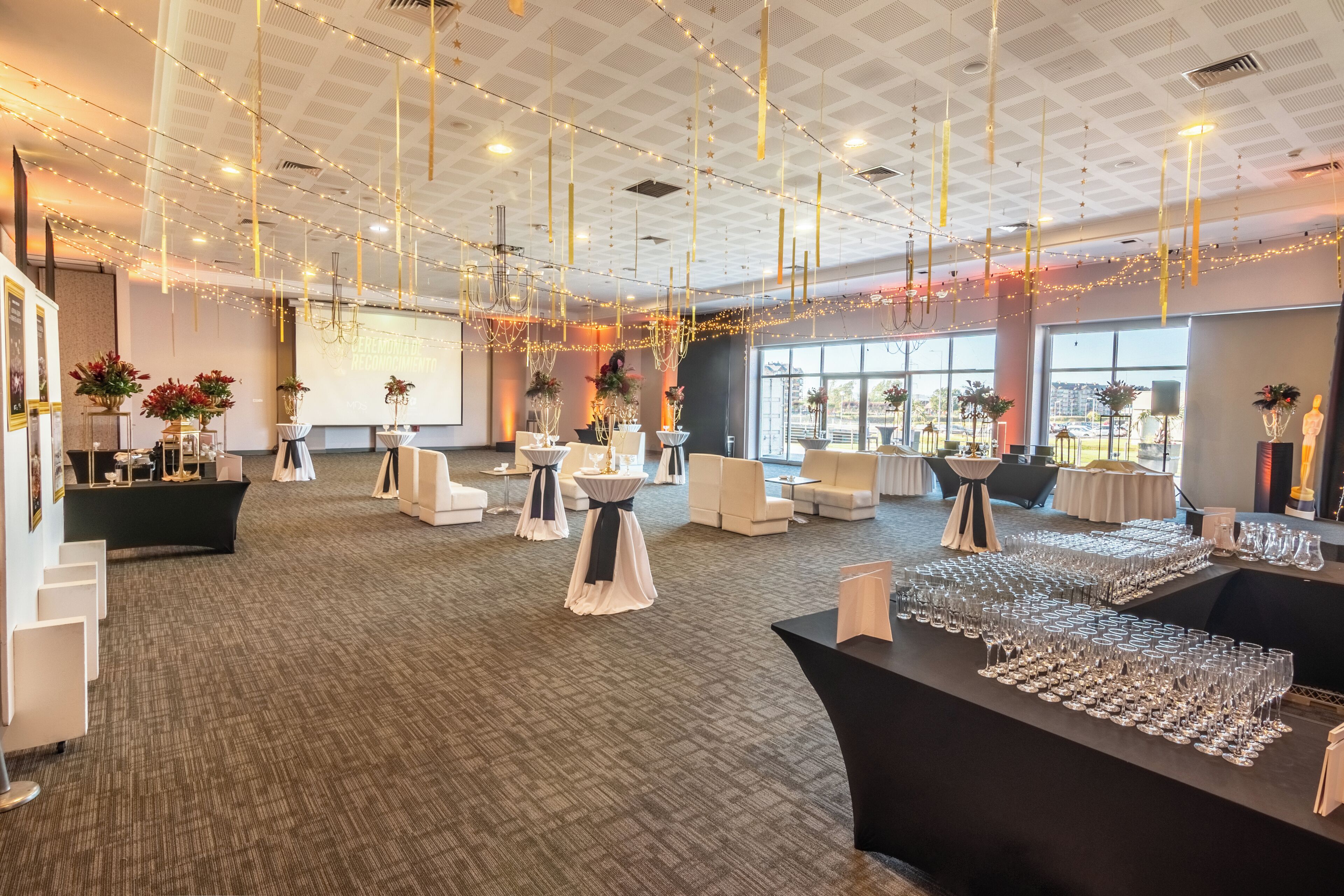 A spacious indoor venue with tables and chairs, string lights, and large windows.