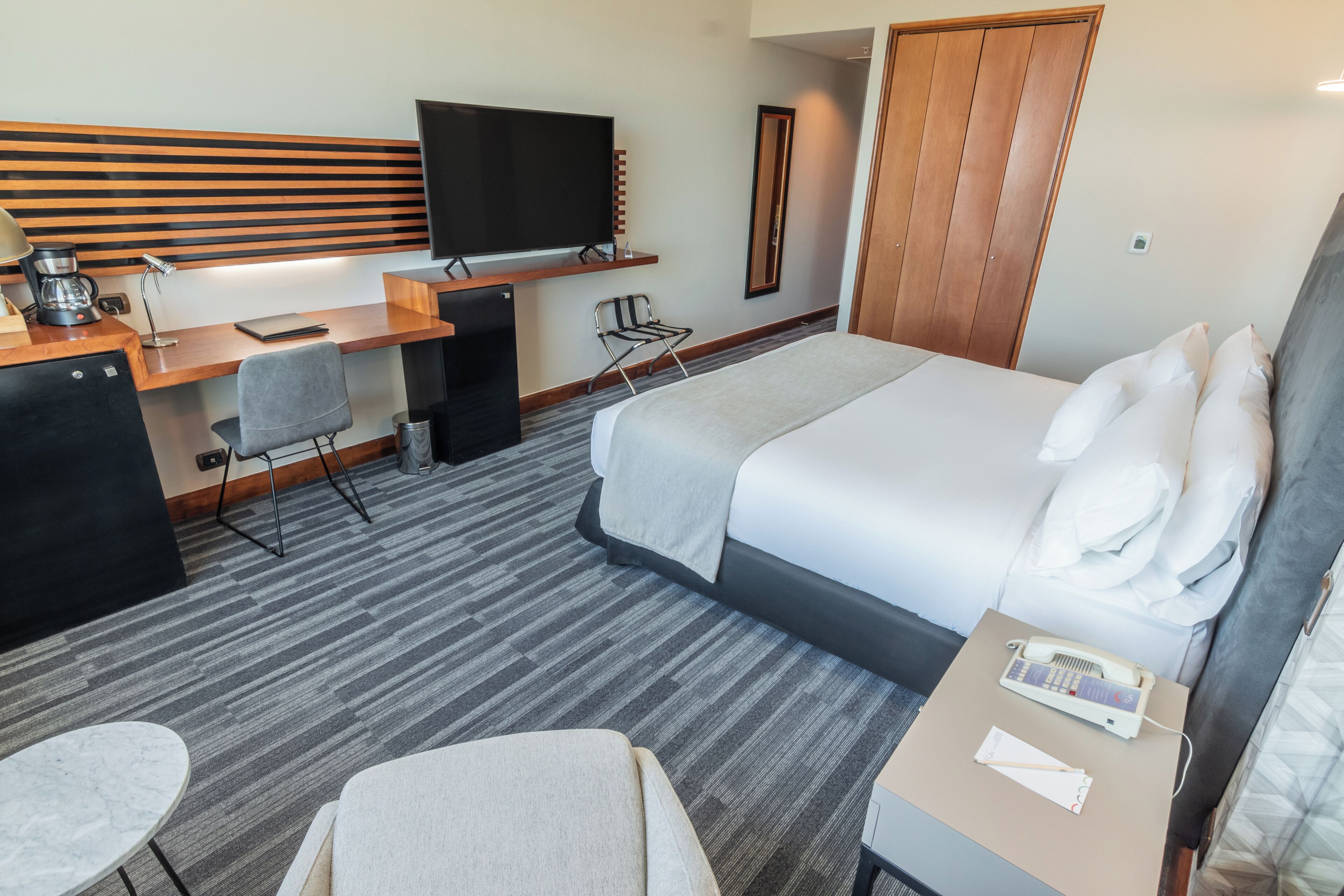 Habitación de hotel con cama, escritorio, silla, televisión y minibar.