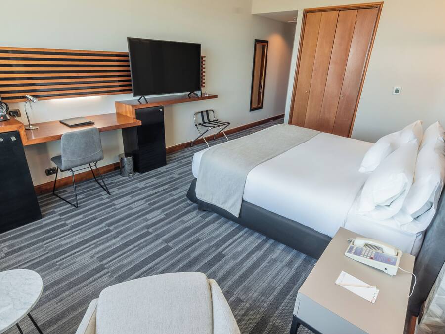 Habitación de hotel con cama, escritorio, silla, televisión y minibar.