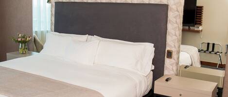 A hotel room with a large bed, a bedside table, a mirror, and a desk with a chair.