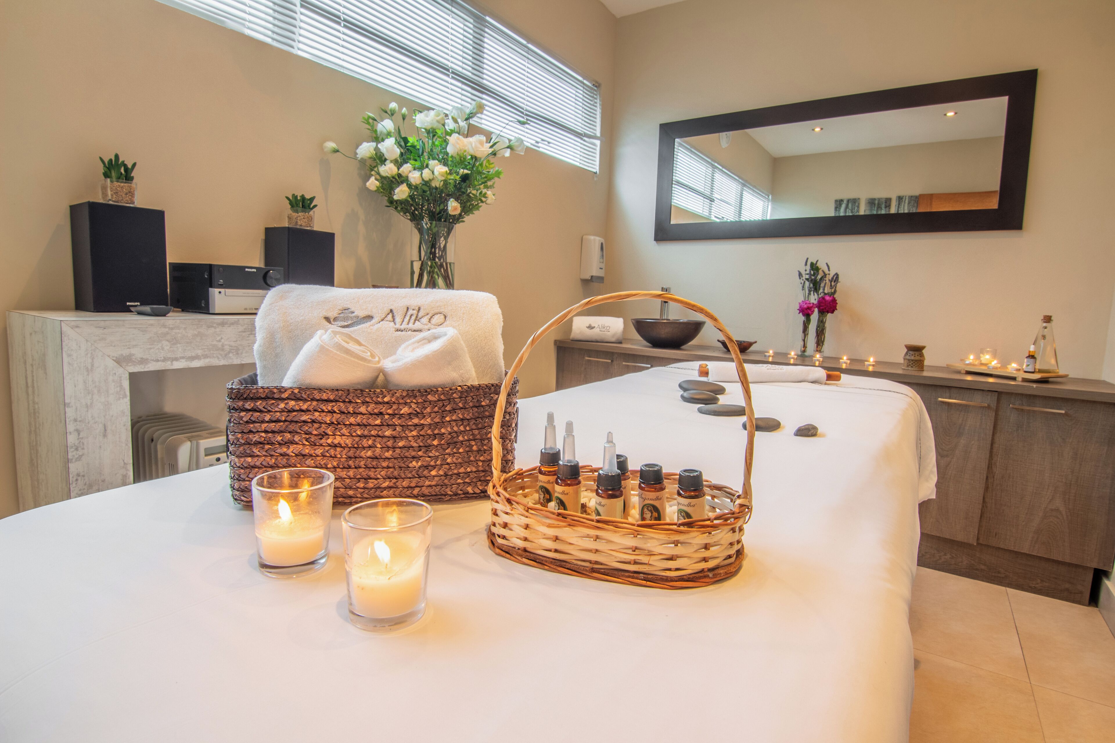 A spa room with a massage table, candles, a basket of toiletries, and a mirror on the wall.