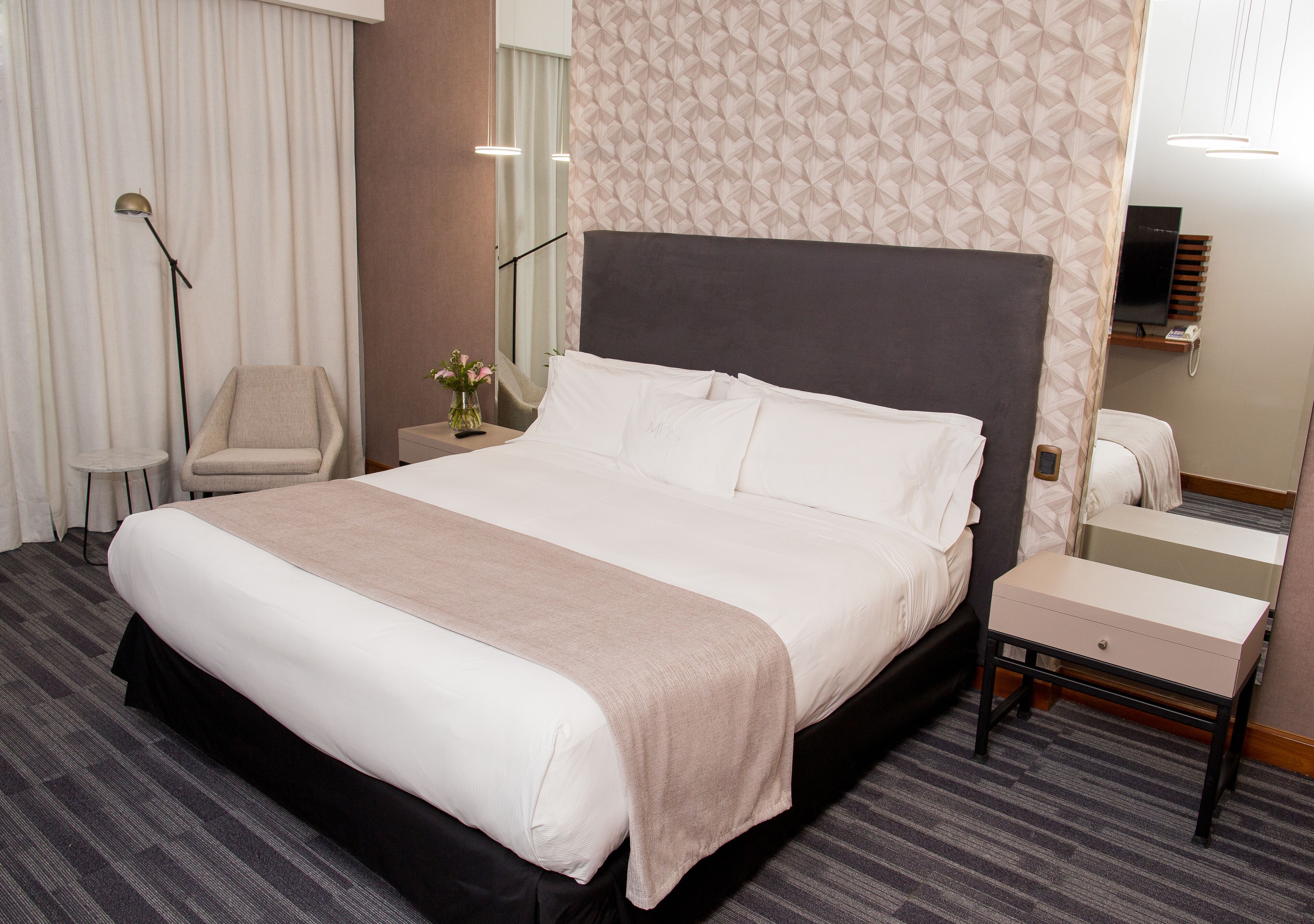 Une chambre d’hôtel avec un grand lit, une table de chevet, une chaise, une lampe et un miroir.