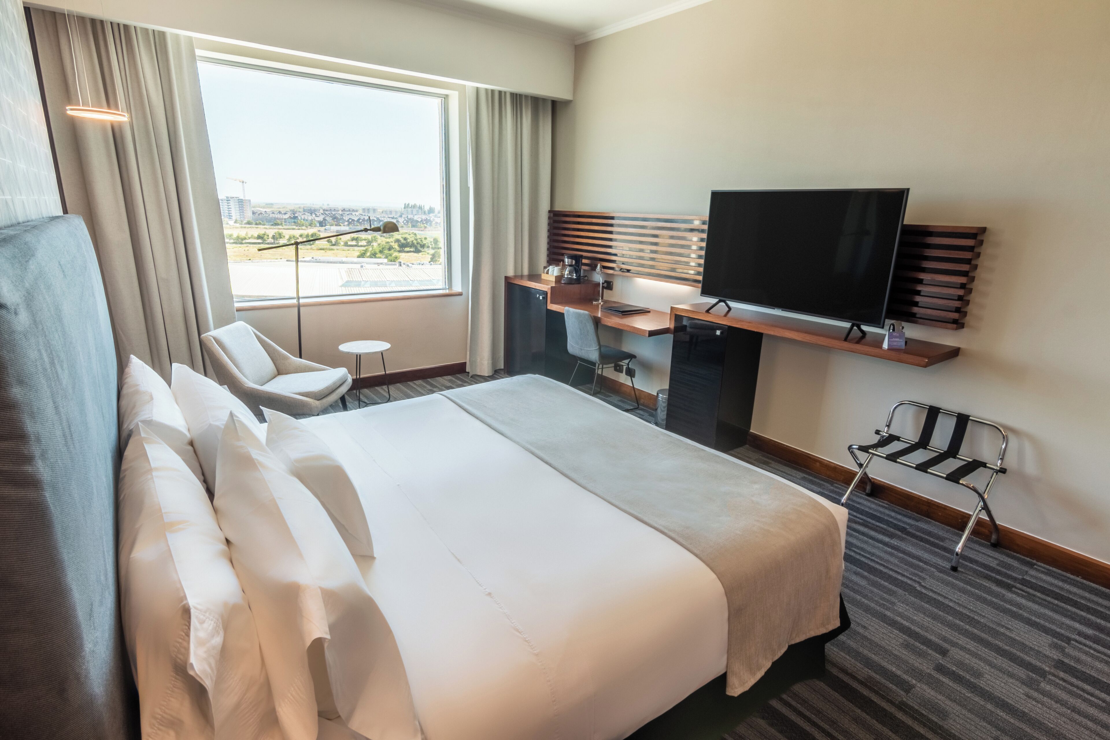 Camera d'albergo con un letto grande, una scrivania con televisore, una sedia e vista sulla città.