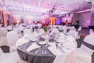 Un salón de banquetes con mesas redondas dispuestas para un evento formal, que incluye manteles blancos, cubertería y centros de mesa florales.