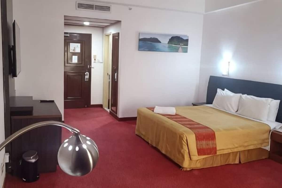 A hotel room with a bed, a desk, a chair, a painting on the wall, and a door leading to another room.