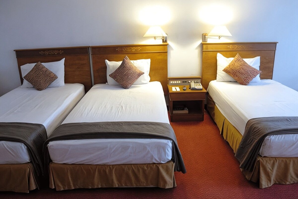 A hotel room with two single beds, each with a wooden headboard, a nightstand, and a lamp.