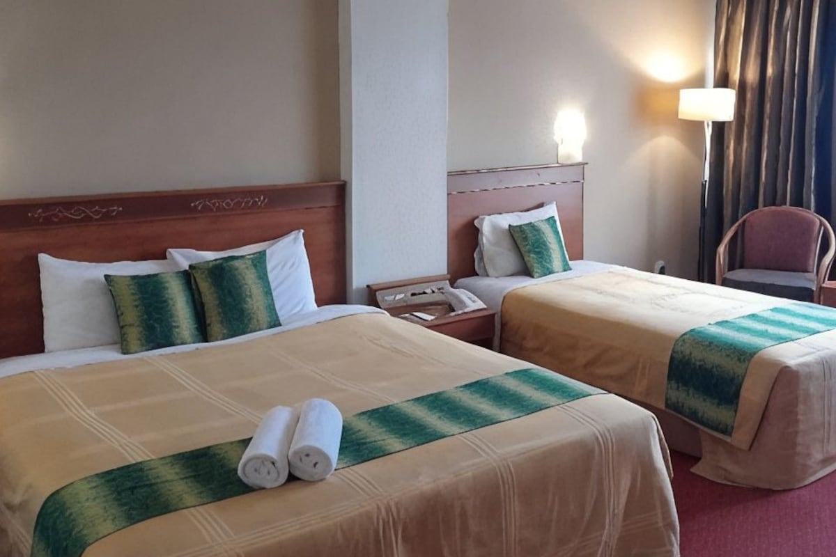 A hotel room with two beds, a nightstand, a lamp, and a chair.