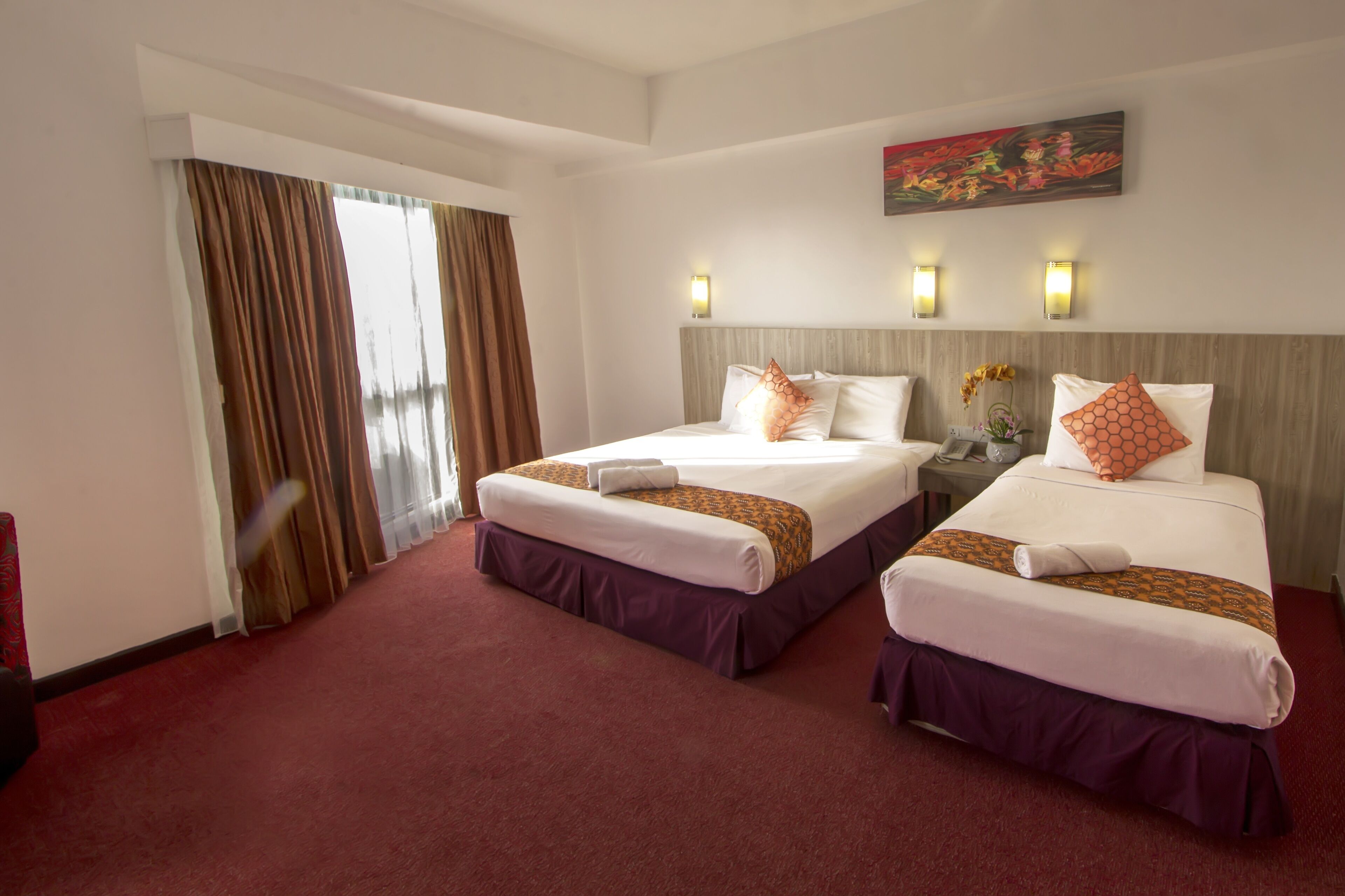A hotel room with two beds, a large window with curtains, and wall-mounted lights.