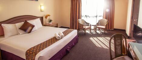 A hotel room with a large bed, a desk with a chair, a television, and a window with curtains.