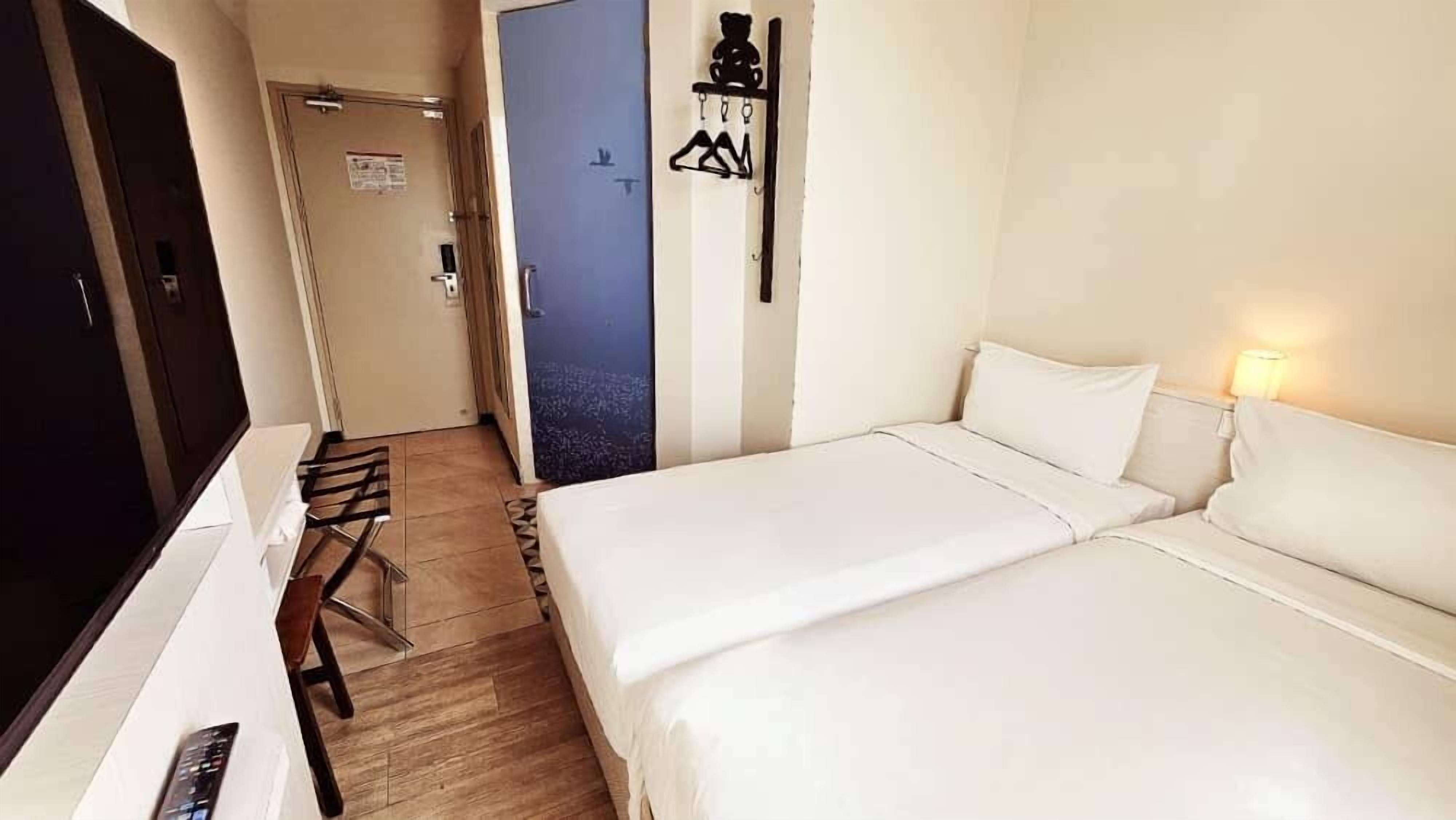 Une chambre d’hôtel comprenant un lit, un bureau avec une télévision, une chaise et un porte-manteau.