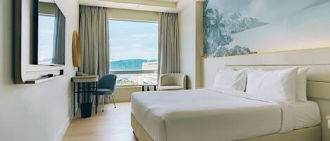 A hotel room with a large bed, a desk with a chair, a TV, and a painting on the wall.
