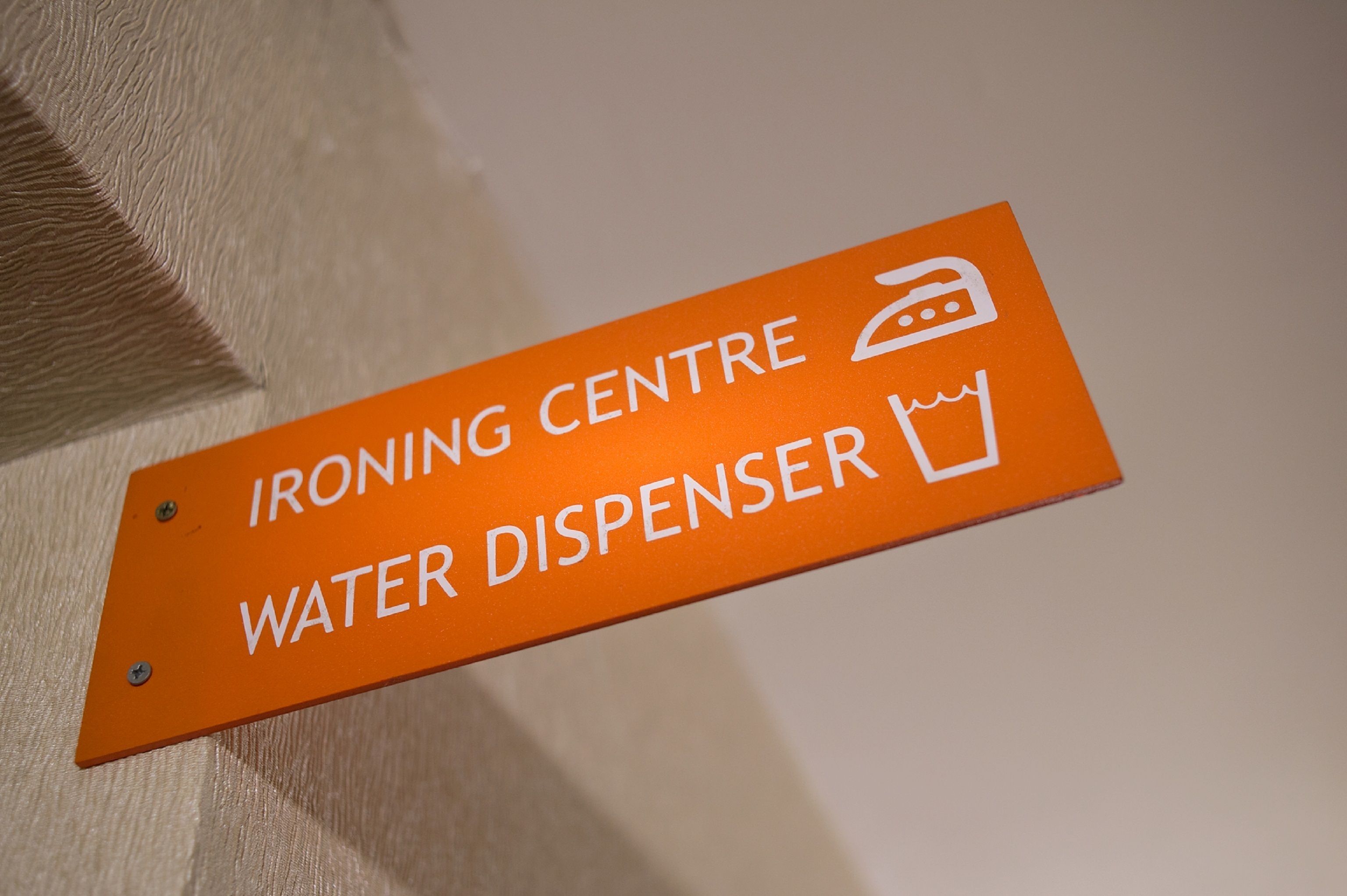 Un letrero naranja con texto blanco que indica una zona de planchado y dispensador de agua.