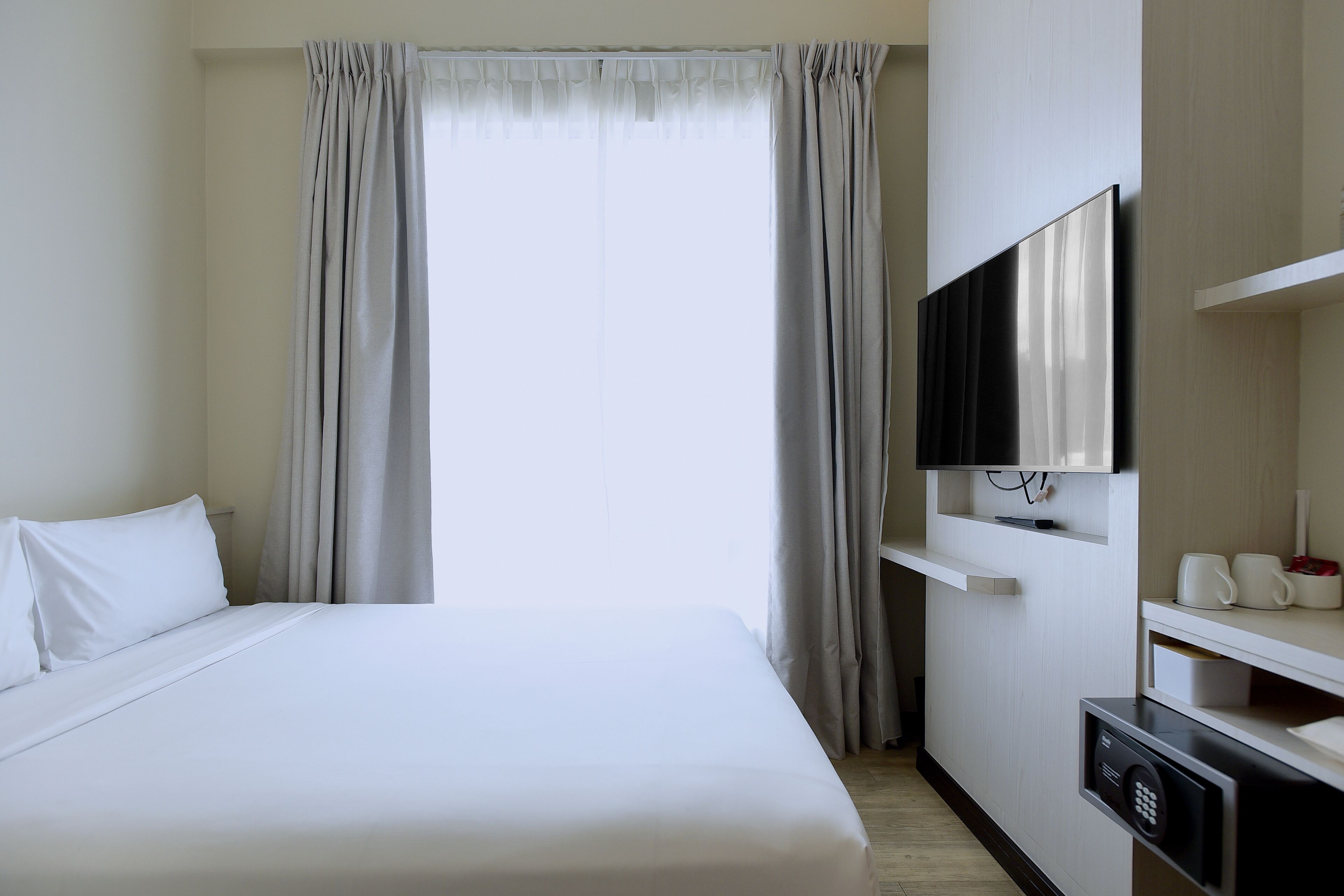 A hotel room with a bed, a TV mounted on the wall, and a window with curtains.