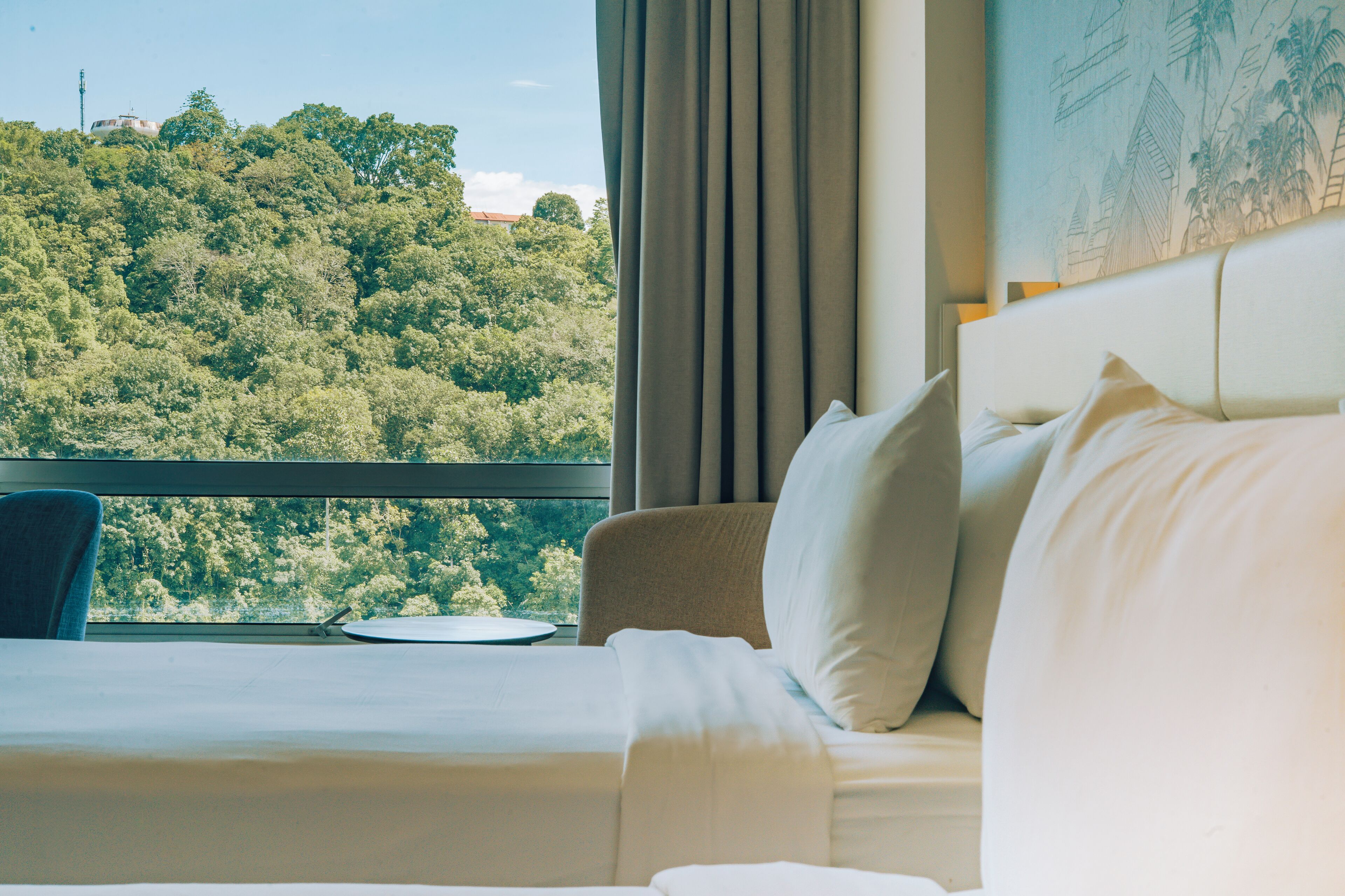 A hotel room with a bed, a chair, and a view of a forested hill.