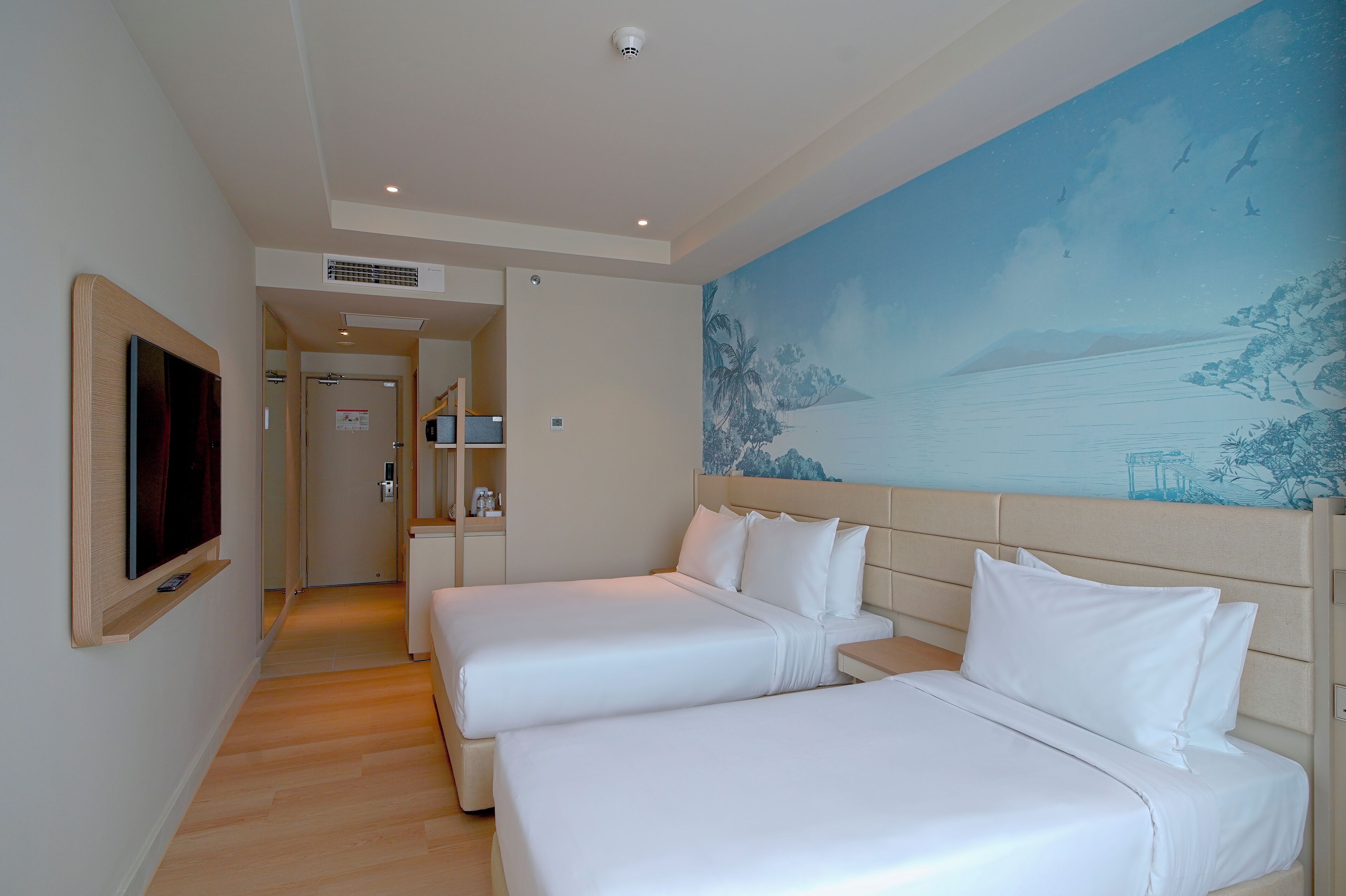 Habitación de hotel con dos camas, un televisor y un cuadro de una escena costera.