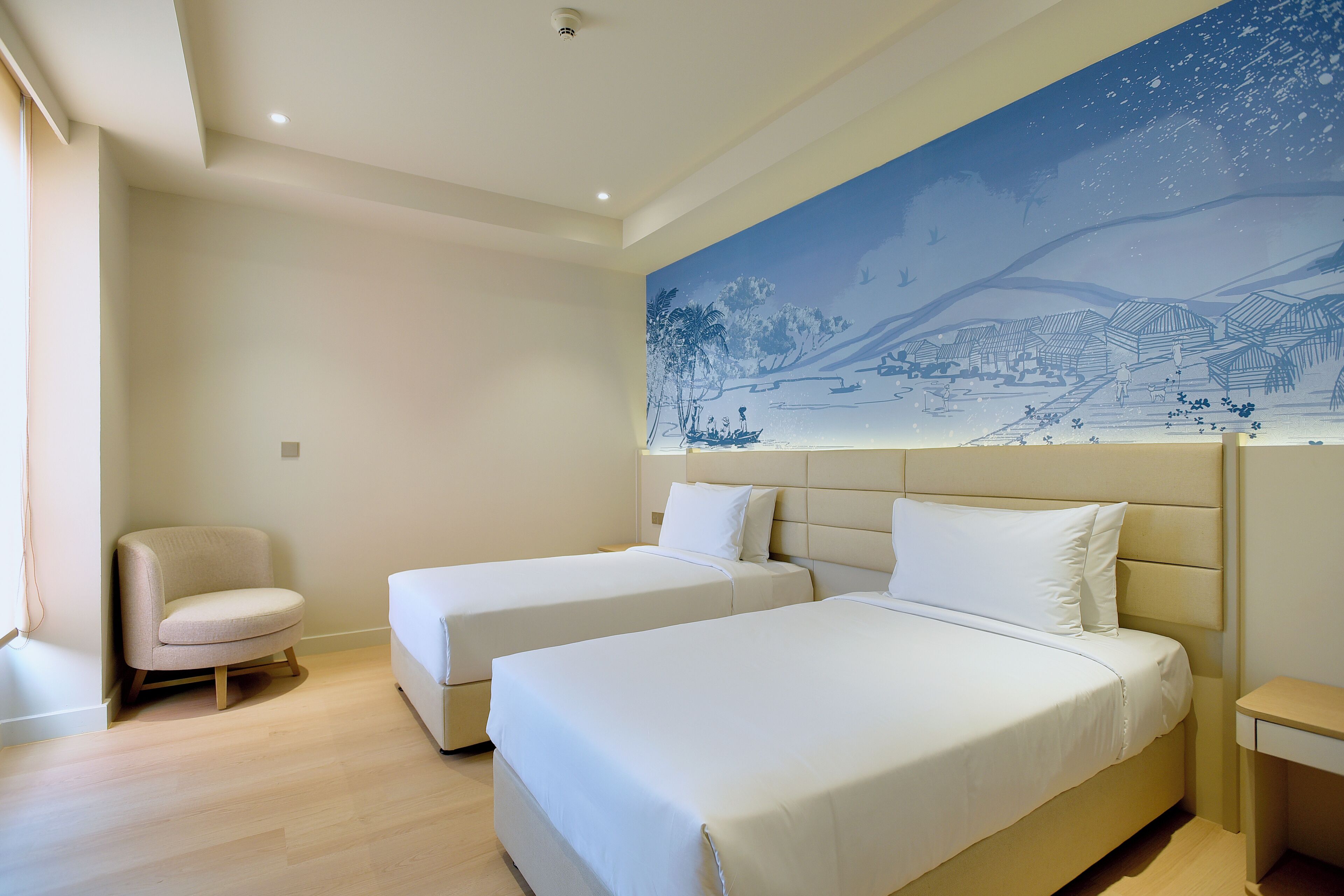 Habitación de hotel con dos camas individuales, una silla y un mural grande en la pared.