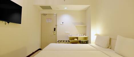 Una habitación de hotel con una cama, un televisor montado en la pared, una mesita de noche y un estante con artículos de aseo.