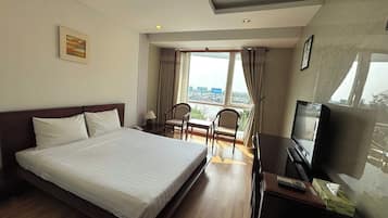 Habitación de hotel con una cama grande, un escritorio con televisor, una silla y vista a la ciudad por la ventana.