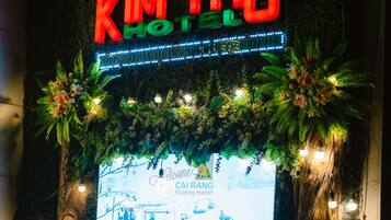 A hotel entrance with a neon sign reading "KIM THO HOTEL" and a large illuminated display of a floating market scene.