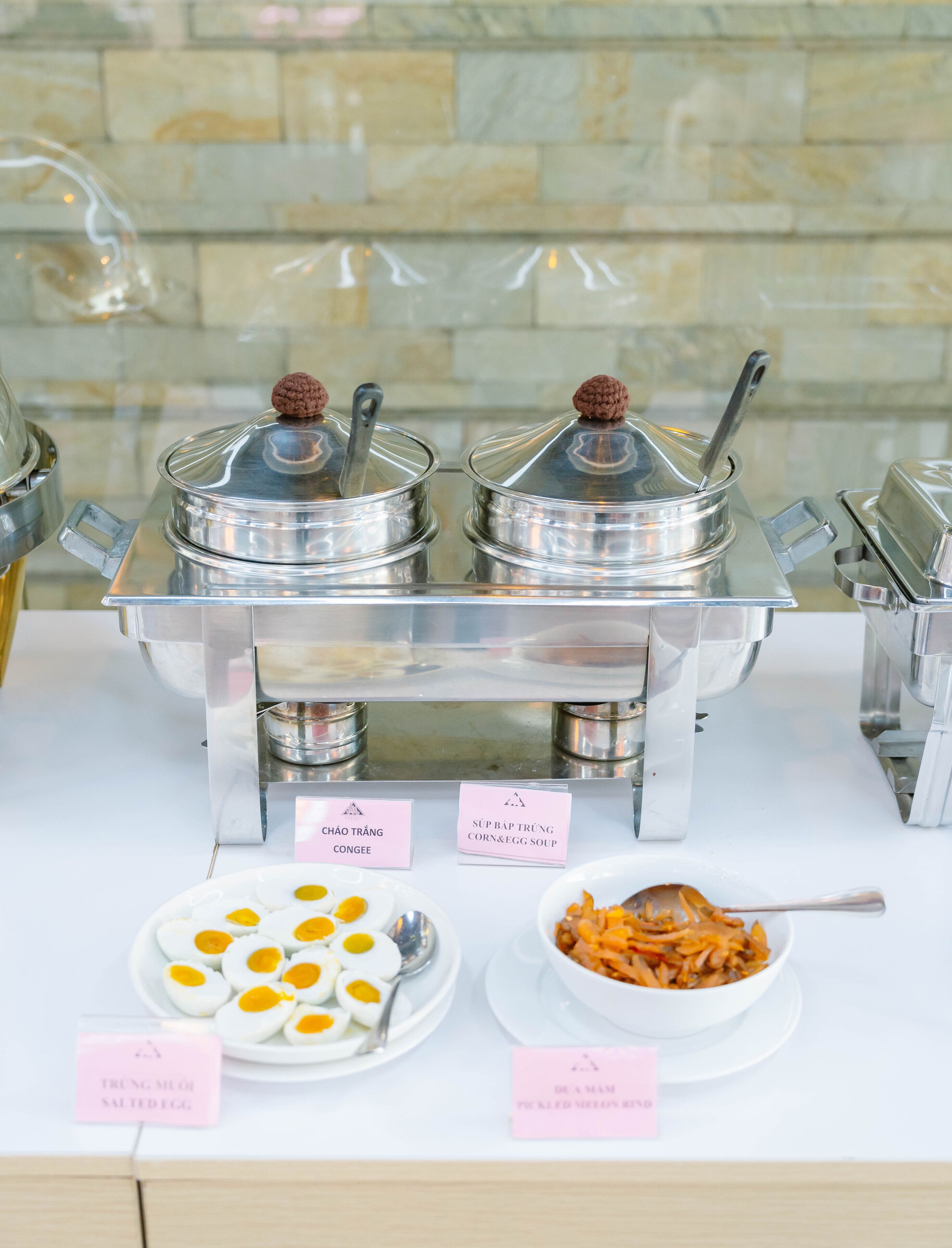 Ein Buffet mit ausgewiesenen Speisen, darunter Congee, Mais- und Eiersuppe, salzgebeizte Eier und eingelegtes Gemüse.