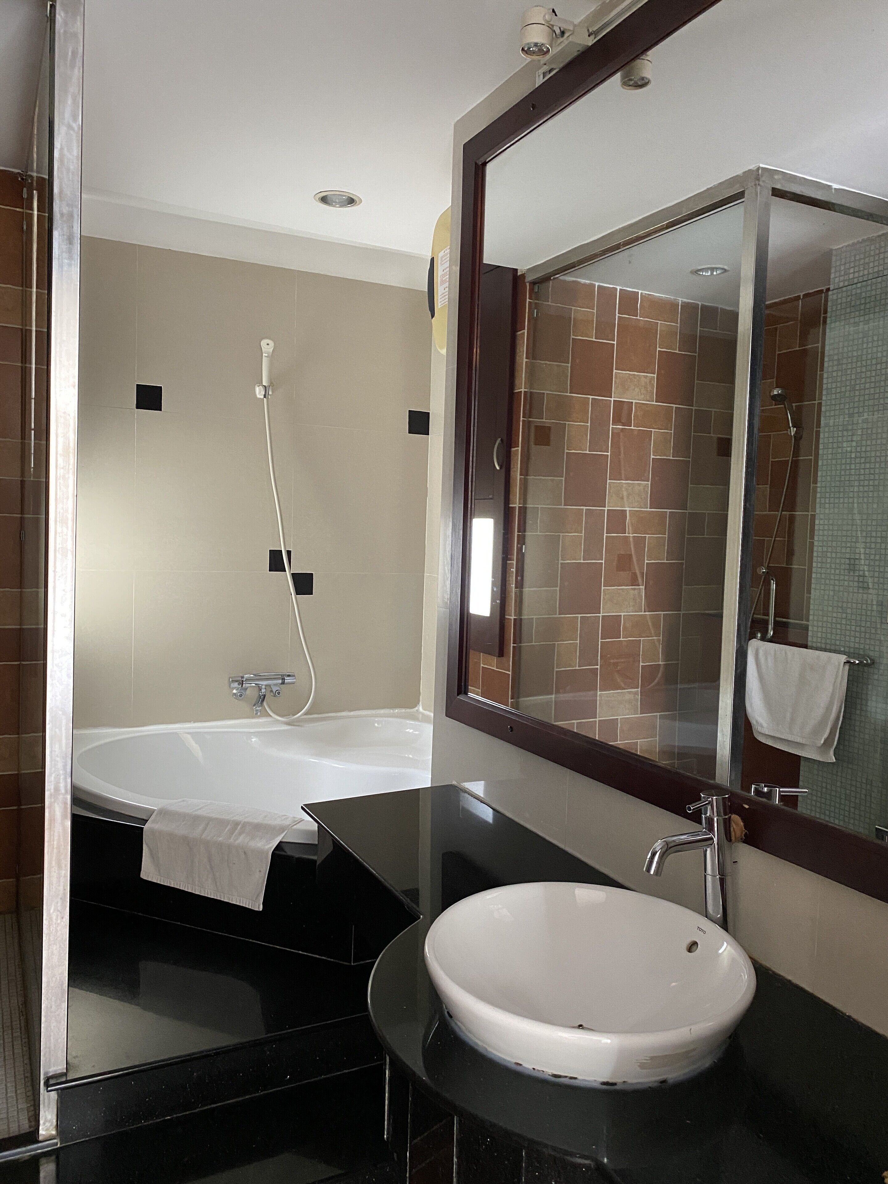 Un baño moderno con un lavamanos negro, una bañera blanca y un espejo grande.