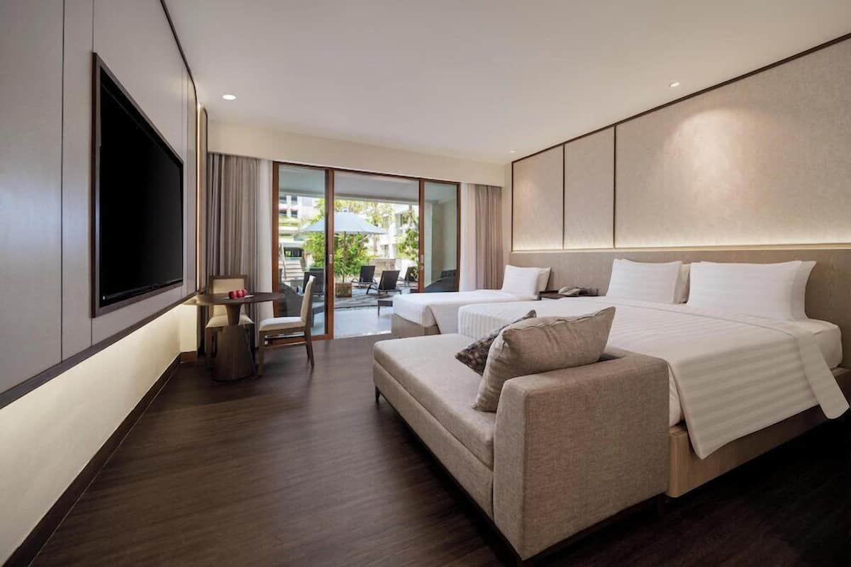 A modern hotel room with a large bed, a sofa, a TV, and a balcony with outdoor seating.