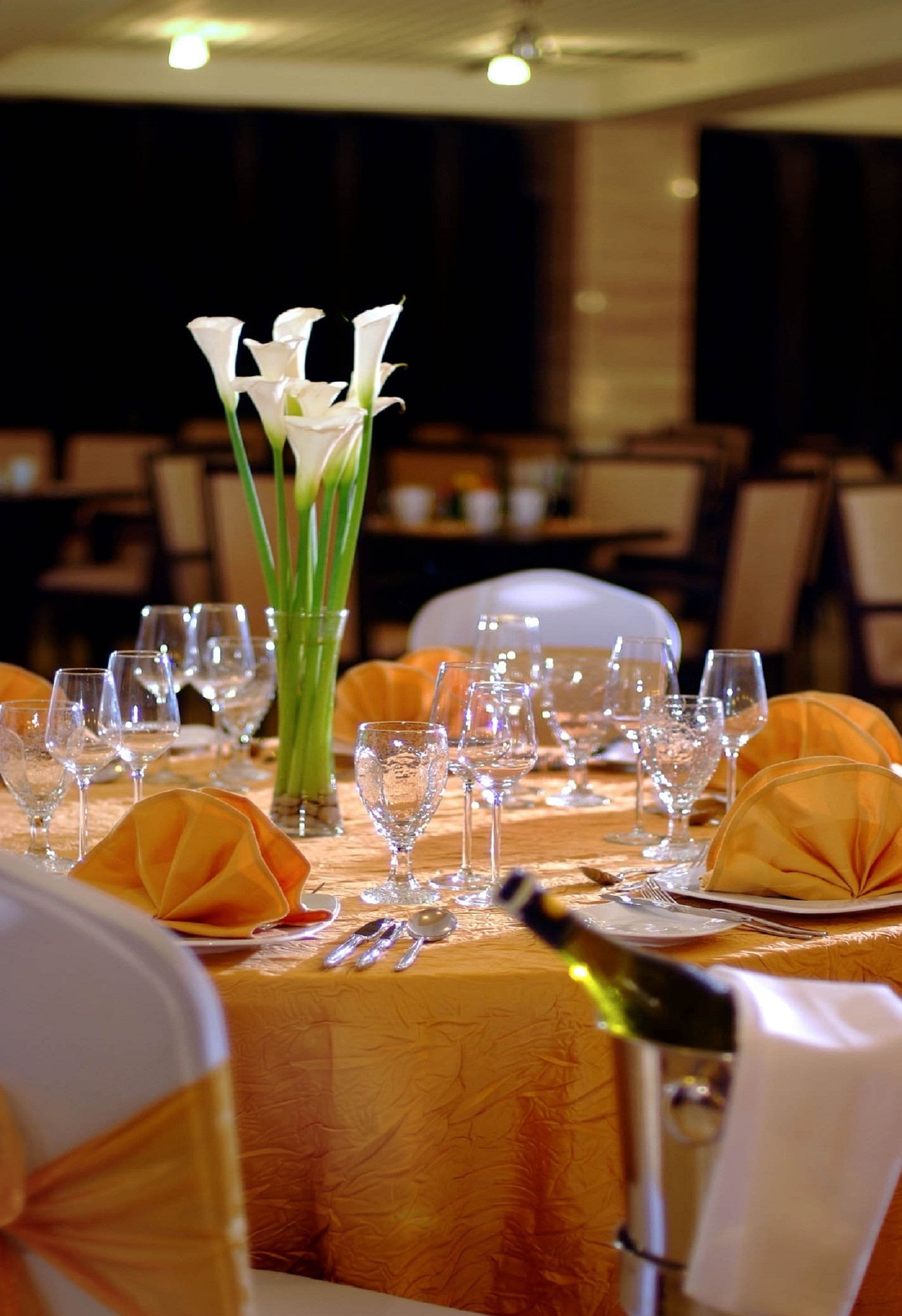 A banquet table set for a formal event with white tablecloths, gold sashes, and a centerpiece of white flowers.