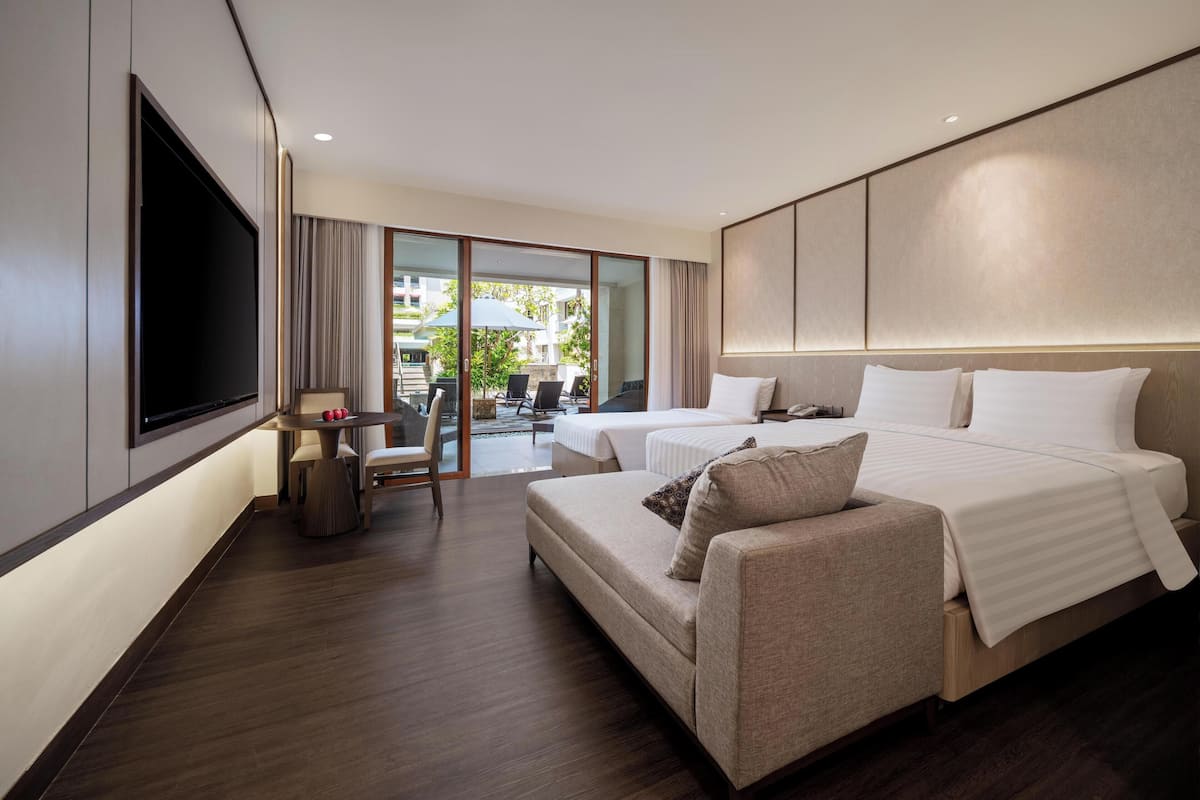 A modern hotel room with a large bed, a sofa, a TV, and a balcony with outdoor seating.