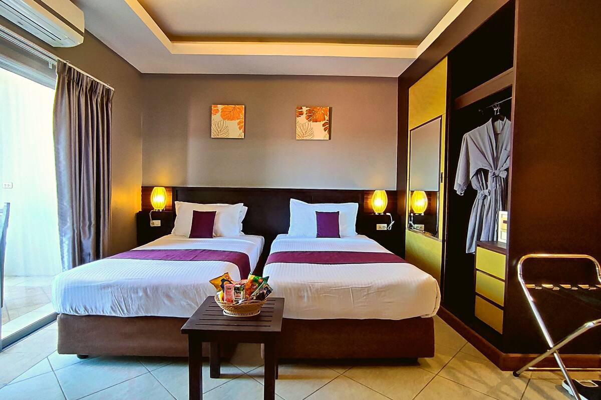 A hotel room with a large bed, two bedside lamps, a small table with a basket, and a robe hanging on the wall.