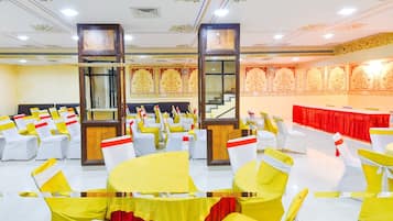 A banquet hall with rows of tables and chairs, ornate ceiling decorations, and a staircase.