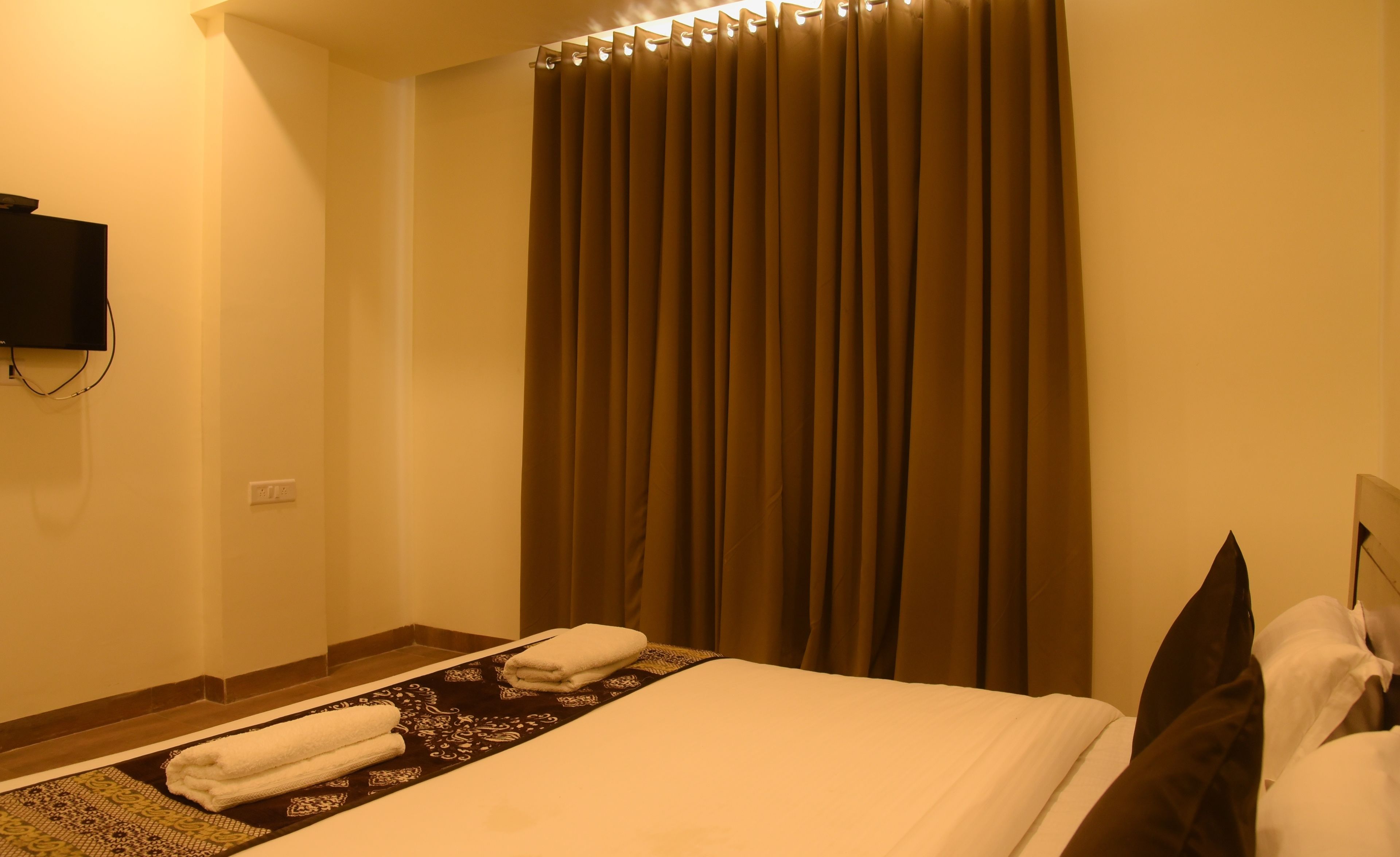 A hotel room with a bed, a flat-screen TV mounted on the wall, a curtain, and a towel rack.