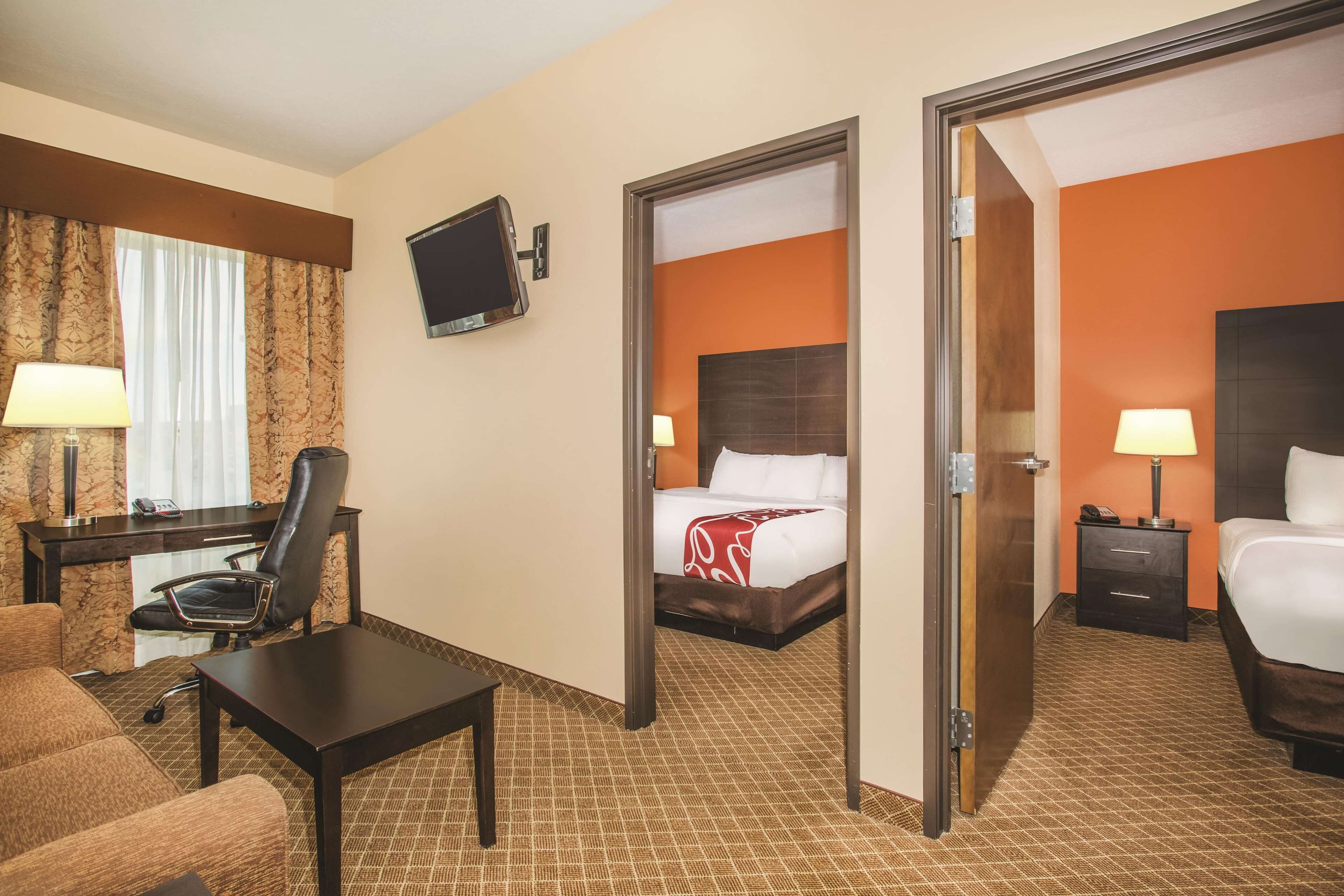 Habitación de hotel con una cama, un escritorio, una silla, un televisor y una puerta que da a otra habitación.