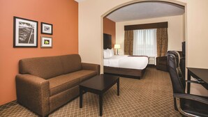 A hotel room with a brown sofa, a small table, a bed with white linens, a desk with a chair, and framed pictures on the wall. - La Quinta Inn & Suites by Wyndham Ely (Ely)